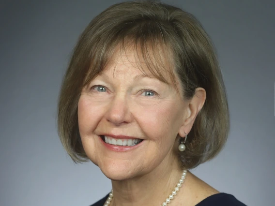 Christine smiling, wearing a black top with pearl earrings and a pearl necklace