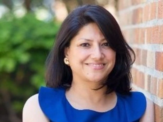 Sunita smiling, with her arms crossed, wearing a blue blouse