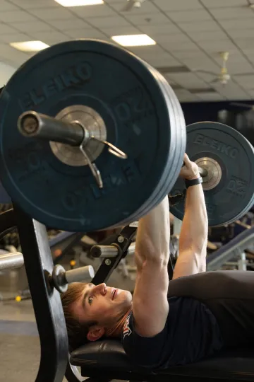A photograph of a man lying on his back, lifting weights over his head