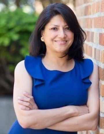 Sunita smiling, with her arms crossed, wearing a blue blouse