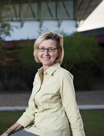 Robin sitting down and smiling, wearing a light-yellow button-up top and gray bottoms